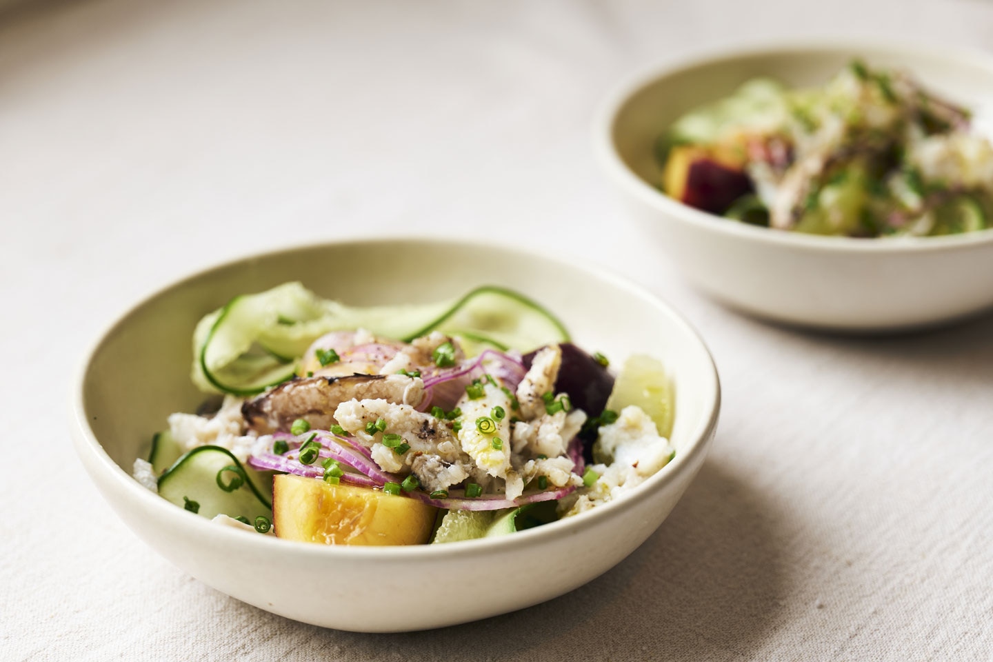 Fresh crab salad topped with avocado slices, cucumber ribbons, lime segments, and peach chunks, served in a bowl and drizzled with olive oil