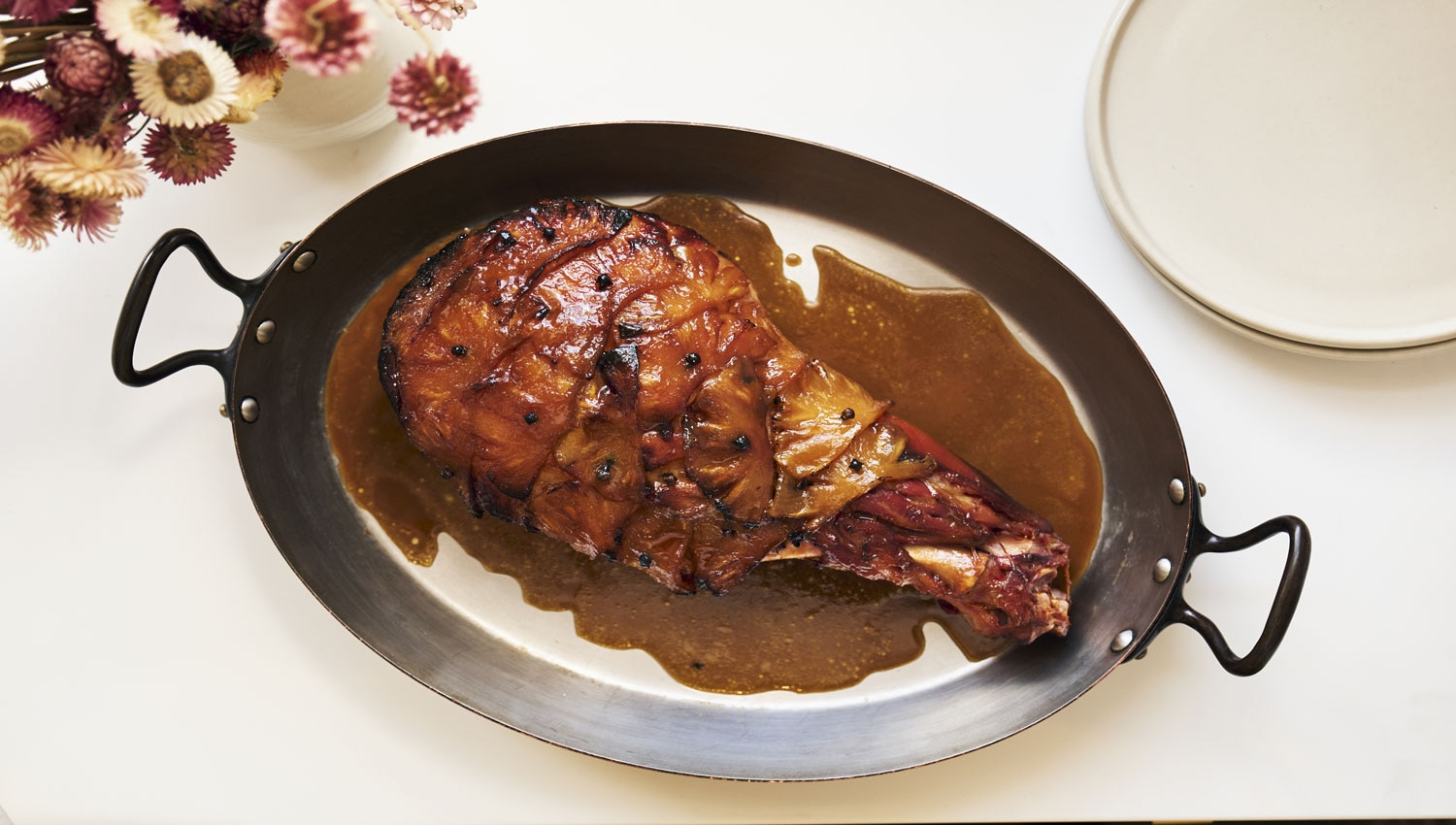 Golden roasted ham topped with caramelized pineapple slices and cloves, glazed with a spiced honey and rum sauce, served on a festive platter