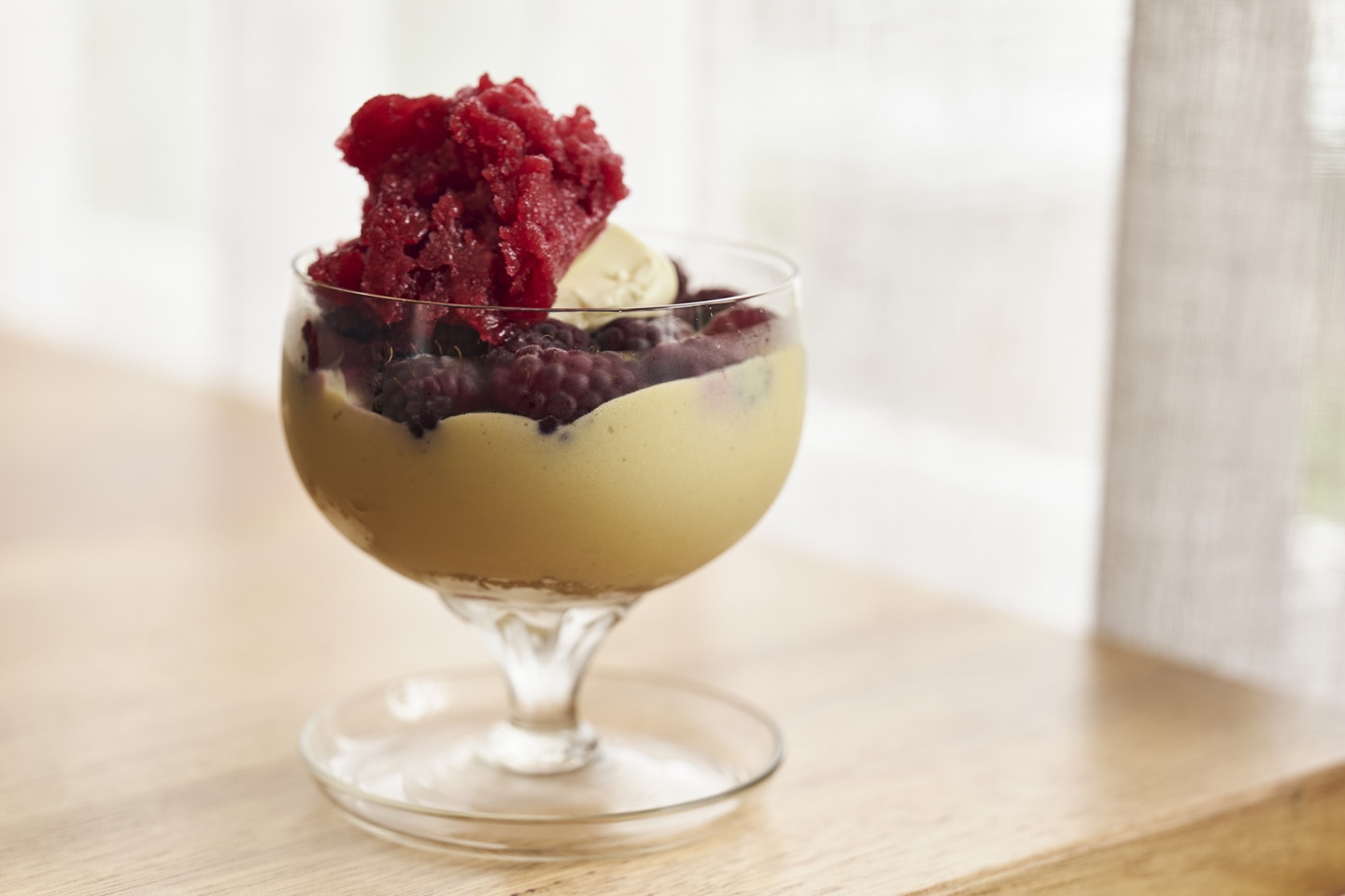 Elegant layered dessert featuring raspberry granita, sponge cake, pastry cream, fresh berries, and whipped cream, beautifully presented in a glass.